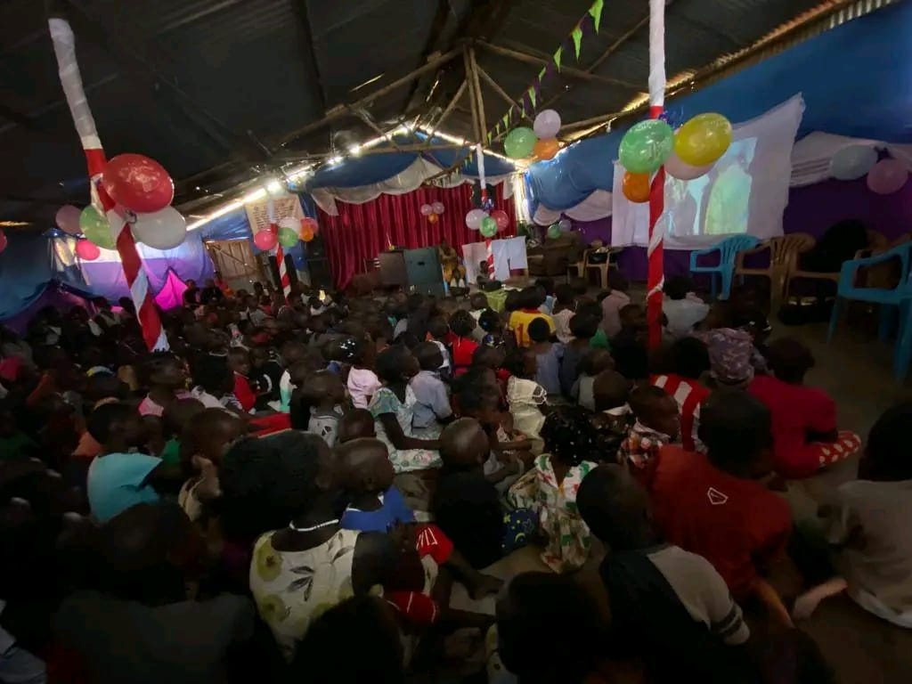 Children gathered under decorated tarpaulin watching a movie screening at the Christmas celebration