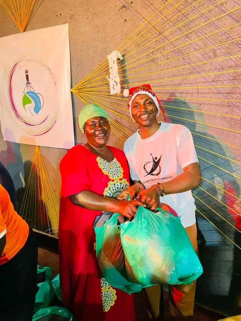 A volunteer in a Santa hat handing a gift bag to a woman in a red dress
