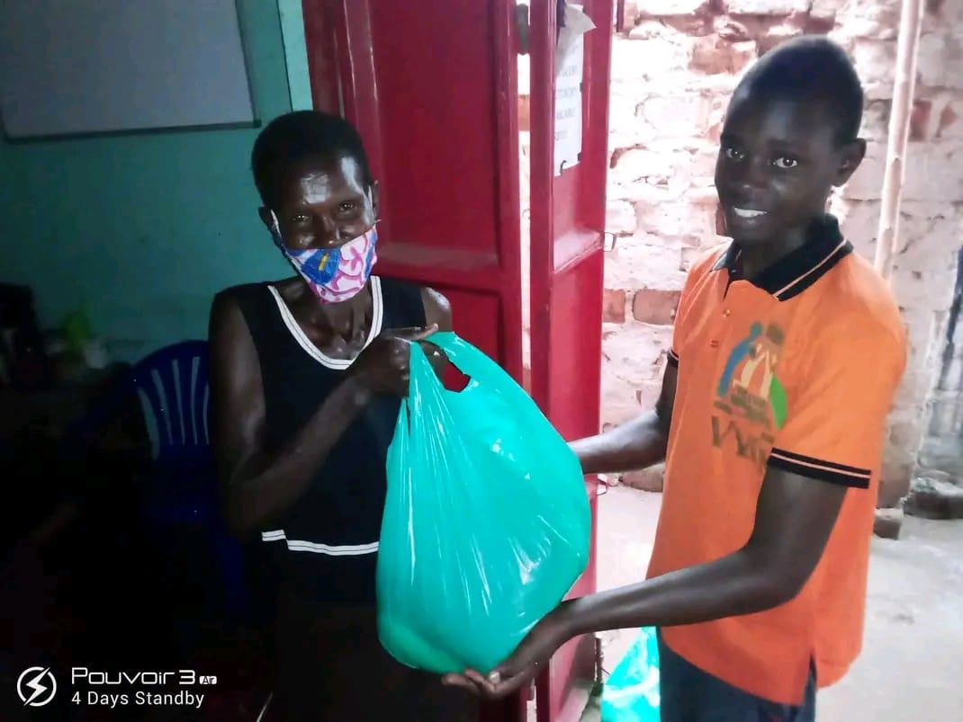 A volunteer handing a bag of relief supplies to a young man outside a home